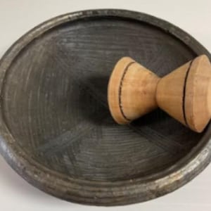 Op de afbeelding: Een donkergrijze vijzel en stamper set. De vijzel is een ondiepe, ronde kom met een textuur. De stamper is gemaakt van lichtgekleurd hout met zwarte accentlijnen. Deze keukentool wordt gebruikt voor het malen en mengen van ingrediënten.