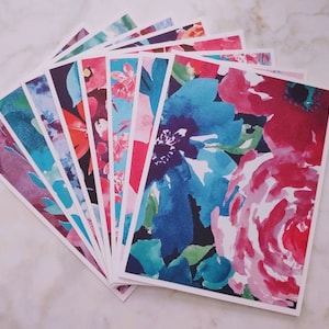 May include: A stack of blank greeting cards with a watercolor floral design featuring pink, blue, and green flowers. The cards are perfect for sending a personalized message to a loved one.