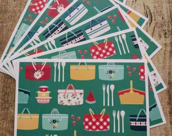 Pode incluir: Um conjunto de oito placemats verdes com tema de cesta de piquenique. Os placemats apresentam um padrão repetitivo de cestas de piquenique, fatias de melancia, morangos e talheres.