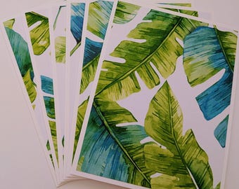 Pode incluir: Um conjunto de cartões brancos com um design em aquarela de folhas tropicais verdes e azuis. As folhas têm uma aparência detalhada e texturizada, com diferentes tons de verde e azul sobre um fundo branco. Os cartões estão dispostos em forma de leque.