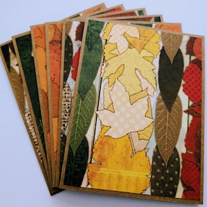 May include: A set of rectangular greeting cards featuring a layered collage of autumn leaves in shades of yellow, orange, red, and dark green. The designs include various textures, patterns, and leaf shapes arranged in vertical columns on a brown cardstock.