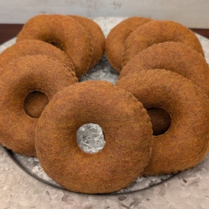 May include: A set of eight brown felt donuts, arranged in a circle on a silver metal surface. The donuts are all the same size and shape, and they have a hole in the center.