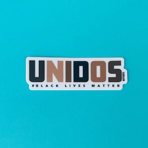 May include: A white sticker with the word "UNIDOS" in black, brown, and tan letters. The text "#BLACK LIVES MATTER" is printed in black below the word "UNIDOS".
