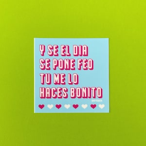 May include: A light blue sticker with pink text that reads "Y SE EL DIA SE PONE FEO TU ME LO HACES BONITO" with a row of white and pink hearts at the bottom and the text "@NYCCOSTA" in smaller pink letters.