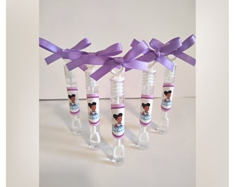 May include: Six clear bubble wands with purple bows. Each wand has a label with a cartoon girl and the text "First Birthday". The wands are arranged in a fan shape against a white background.