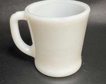 May include: A white, opaque mug with a curved handle. The mug has a slightly flared shape, wider at the top than the base. The mug is made of a solid, smooth material.