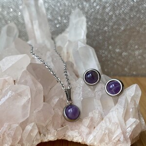 May include: A silver necklace and earrings set with a purple amethyst stone pendant and matching earrings.