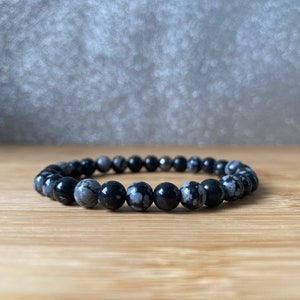 K&ouml;nnte beinhalten: Ein Armband aus schwarzen und wei&szlig;en, gefleckten Steinperlen. Das Armband besteht aus runden Perlen und hat einen silbernen Metallverschluss.