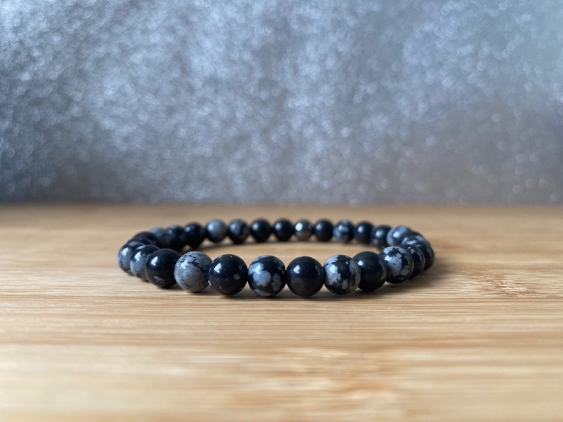 K&ouml;nnte beinhalten: Ein Armband aus schwarzen und wei&szlig;en, gefleckten Steinperlen. Das Armband besteht aus runden Perlen und hat einen silbernen Metallverschluss.