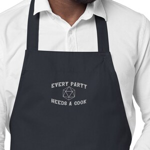 May include: A dark blue apron with white embroidery that reads "Every Party Needs A Cook" and features a white outline of a 20-sided die.