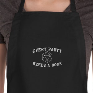May include: Black apron with white embroidery that reads "Every Party Needs A Cook" and a white outline of a twenty-sided die.