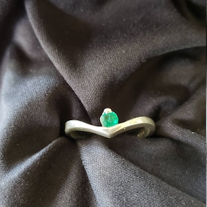Könnte beinhalten: Ein silberner Ring mit einem grünen Edelstein in der Mitte. Der Ring ist V-förmig.