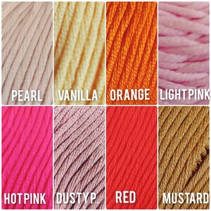 Op de afbeelding: Een verzameling garenklossen in verschillende kleuren, waaronder parel, vanille, oranje, lichtroze, roze, stoffig roze, rood en mosterd.