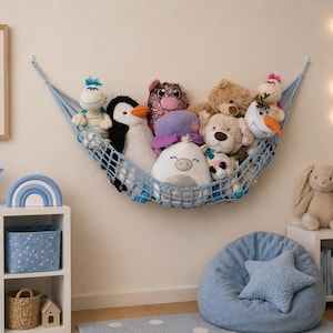 May include: A blue mesh toy hammock is filled with soft toys. A framed bear picture, a star light, and a rainbow decoration sit on a white shelf. A blue beanbag chair with a star cushion is in the foreground.