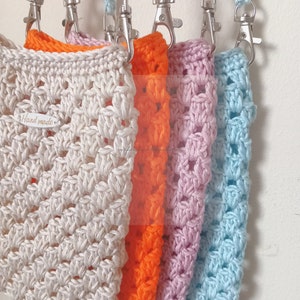 Op de afbeelding: Vijf gehaakte tassen in verschillende kleuren, waaronder cr&egrave;me, oranje, roze en lichtblauw, met zilveren sluitingen en bijpassende banden. De cr&egrave;mekleurige tas heeft een "Hand Made"-label.