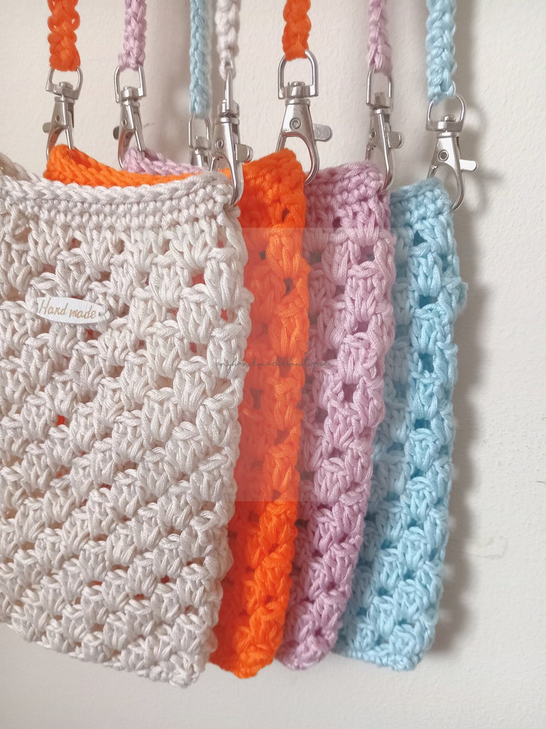 Op de afbeelding: Vijf gehaakte tassen in verschillende kleuren, waaronder cr&egrave;me, oranje, roze en lichtblauw, met zilveren sluitingen en bijpassende banden. De cr&egrave;mekleurige tas heeft een "Hand Made"-label.