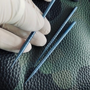 Puede incluir: Tres herramientas de metal azul con una superficie texturizada. Las herramientas son delgadas y largas con extremos puntiagudos.