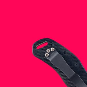 May include: Black folding knife with a textured handle and a black pocket clip. The handle is secured with small silver screws. The knife is set against a bright pink background.