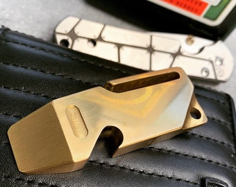 Könnte beinhalten: Ein goldfarbenes Multitool aus Metall mit einem Flaschenöffner und einem Brecheisen. Das Werkzeug liegt auf einer schwarzen Lederbörse mit einem genähten Muster.
