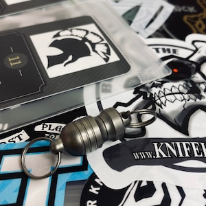 May include: A silver key chain with a magnetic clasp and a silver ring. The keychain is lying on top of a variety of colorful stickers and patches.