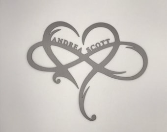 May include: A silver metal infinity symbol with a heart shape in the center. The names "Andrea" and "Scott" are written inside the heart.