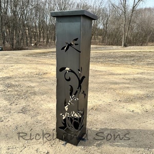 May include: A black metal garden sculpture with a dragonfly and floral design. The sculpture is tall and slender, with a square base.