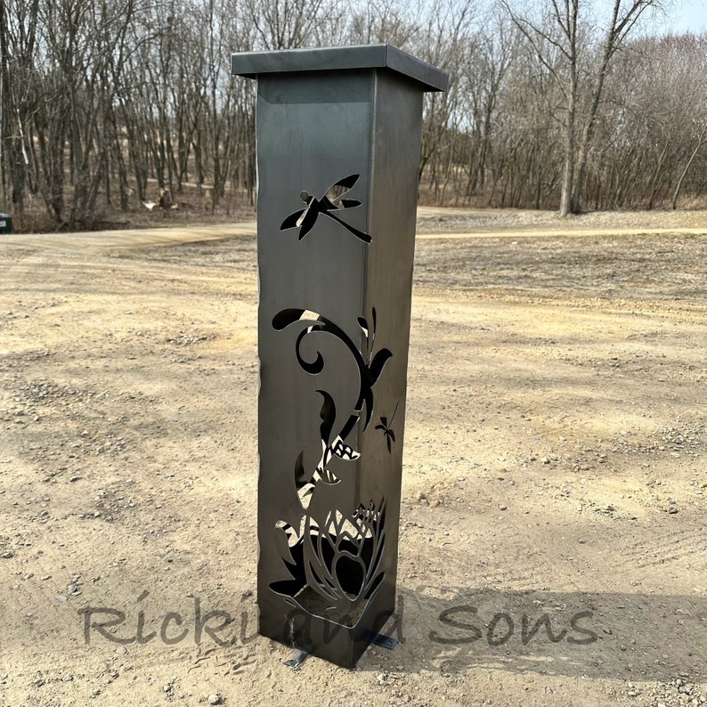 May include: A black metal garden sculpture with a dragonfly and floral design. The sculpture is tall and slender, with a square base.