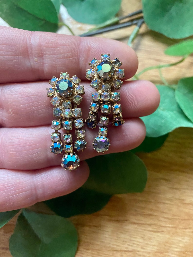 May include: A pair of vintage gold-toned earrings with iridescent, teardrop-shaped crystals. Each earring features a floral-shaped top with a large central stone and dangling crystal accents, creating a glamorous, eye-catching design.