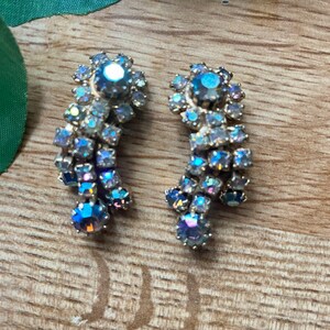 May include: A pair of vintage, iridescent rhinestone earrings. Each earring features a cluster of small, shimmering stones in shades of blue, purple, and silver, arranged in a cascading design. The earrings have a gold-tone metal setting.