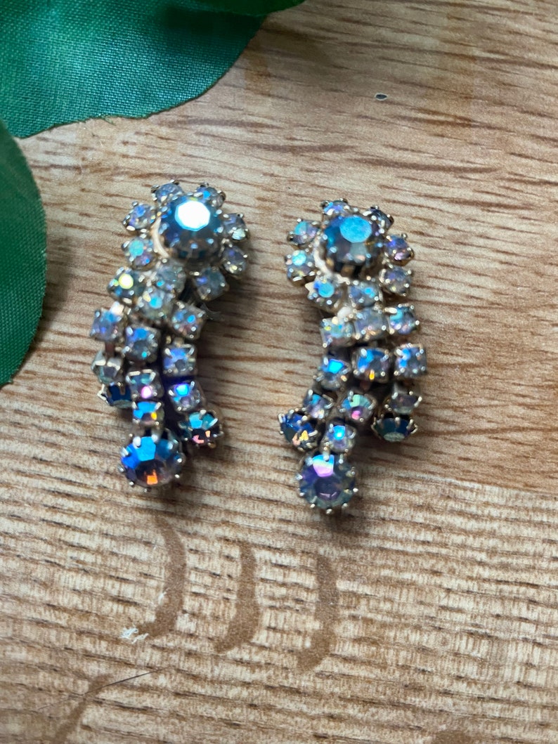 May include: A pair of vintage, iridescent rhinestone earrings. Each earring features a cluster of small, shimmering stones in shades of blue, purple, and silver, arranged in a cascading design. The earrings have a gold-tone metal setting.