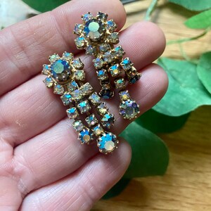 May include: Vintage gold-toned earrings with iridescent, teardrop-shaped rhinestones. The earrings feature a cluster of stones at the top and a cascading design of smaller stones, creating a glamorous, eye-catching accessory.