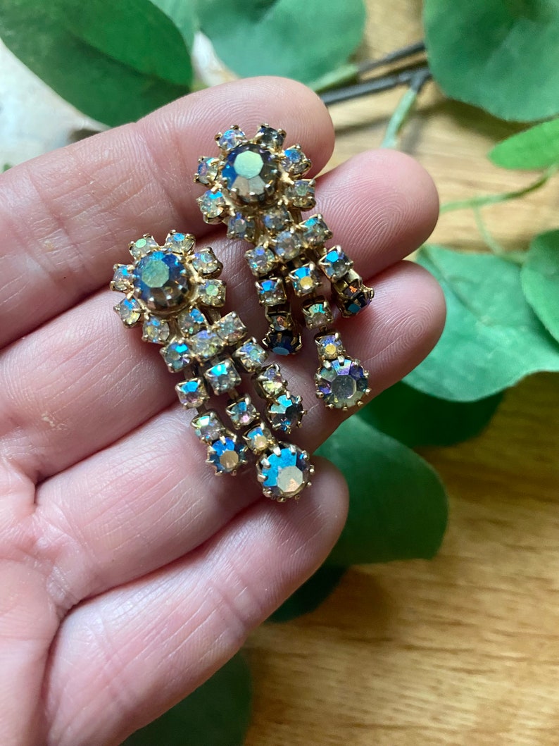 May include: Vintage gold-toned earrings with iridescent, teardrop-shaped rhinestones. The earrings feature a cluster of stones at the top and a cascading design of smaller stones, creating a glamorous, eye-catching accessory.