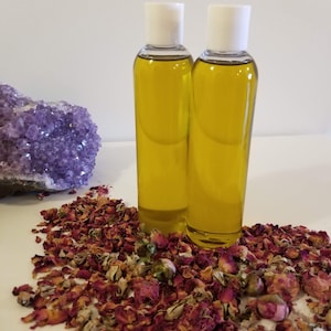 May include: Two clear glass bottles with white lids filled with a yellow liquid, sitting on a white surface surrounded by dried rose petals.