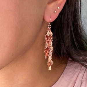 May include: Rose gold dangle earrings featuring a cascade of small leaf charms.