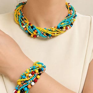 May include: A multi-strand beaded necklace and matching bracelet set featuring a vibrant mix of small and medium-sized beads in bright yellow, turquoise blue, black, white, and orange, arranged in a twisted, layered design.