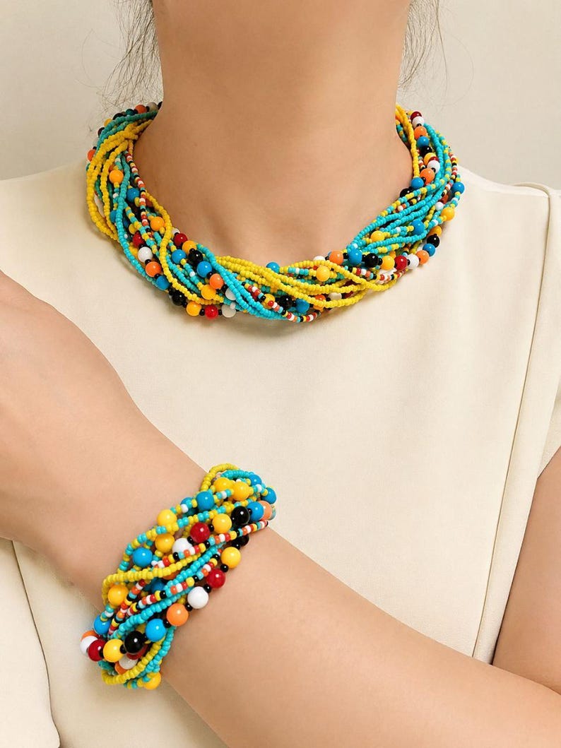 May include: A multi-strand beaded necklace and matching bracelet set featuring a vibrant mix of small and medium-sized beads in bright yellow, turquoise blue, black, white, and orange, arranged in a twisted, layered design.