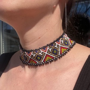May include: A beaded choker necklace with a geometric pattern in black, white, red, gold, and blue.