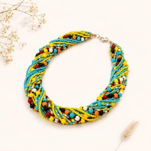 May include: A multi-strand statement necklace composed of twisted turquoise, yellow, orange, red, black, and white seed beads. The necklace features a silver-toned metal lobster claw clasp and a short extender chain for adjustable length and secure closure.