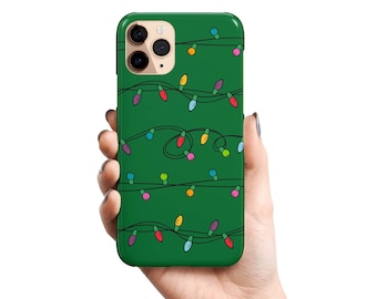 May include: Green phone case with a festive design of colorful Christmas lights. The case features a repeating pattern of red, yellow, blue, and pink bulbs strung on black wires, creating a holiday theme. The phone case is held in a hand.