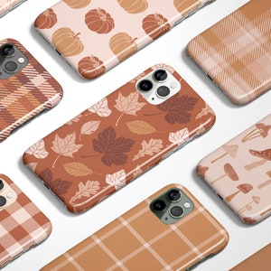 May include: A collection of phone cases with autumn-themed designs. Patterns include pumpkins, leaves, mushrooms, and plaid in shades of brown, beige, and cream. The cases are arranged on a white background.