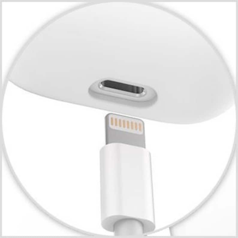 May include: Close-up of a white charging case with a Lightning connector port. A white Lightning cable is plugged into the port.