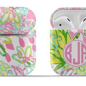 May include: A pink, green, and yellow floral patterned Airpods case with a silver keychain and a pink circle with the monogram "BJA" in white.