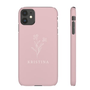 May include: A pink phone case with a white floral design and the name "KRISTINA" printed on the back.