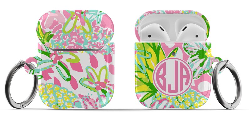 May include: A white Airpods case with a pink, green, and yellow floral pattern. The case has a silver carabiner clip and a pink circle with the monogram "BJA" in white.