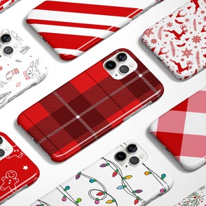 May include: A collection of smartphone cases with festive Christmas-themed designs. The cases feature patterns like red and white stripes, plaid, reindeer, gingerbread men, and string lights. The cases are in various shades of red, white, and green.