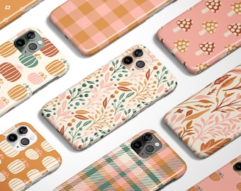May include: A collection of phone cases with various fall-themed designs. Patterns include pumpkins, mushrooms, plaid, and floral arrangements in shades of orange, pink, green, and cream. The cases are arranged on a white surface.