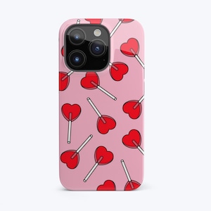 Puede incluir: Una funda rosa para iPhone con un patr&oacute;n de piruletas rojas en forma de coraz&oacute;n. La funda tiene un recorte para el objetivo de la c&aacute;mara.