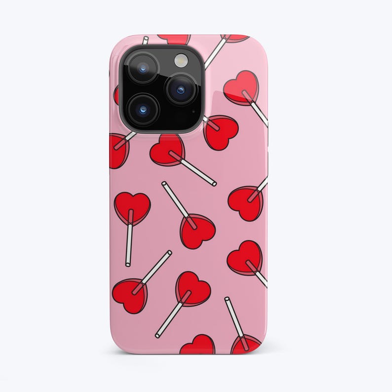 Puede incluir: Una funda rosa para iPhone con un patr&oacute;n de piruletas rojas en forma de coraz&oacute;n. La funda tiene un recorte para el objetivo de la c&aacute;mara.