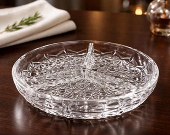 May include: A clear, round, divided serving dish with a textured, starburst pattern. The dish is made of glass and has three sections, perfect for serving appetizers or snacks. The dish sits on a dark wooden surface.