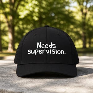 May include: Black baseball cap with the text "Needs supervision." in white. The cap has a mesh back and a curved brim. The hat is a classic style, suitable for casual wear.